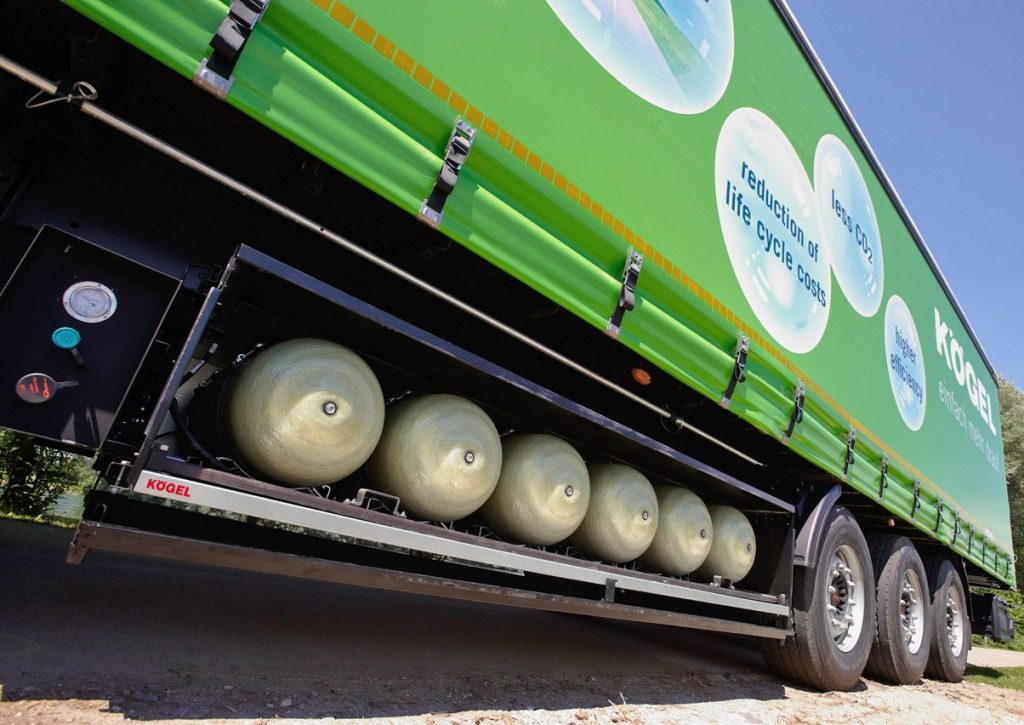 Sześć cylindrycznych zbiorników CNG zamontowanych pod zieloną naczepą Kögel, obok grafika reklamowa o niższych kosztach eksploatacji