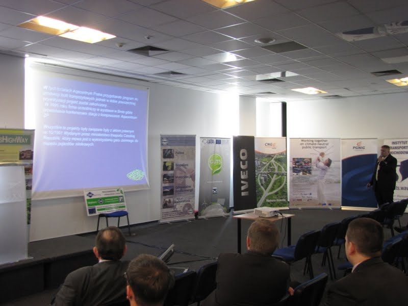 Sala konferencyjna z roll-upami sponsorów IVECO i PGNiG, prelegent przemawiający do publiczności