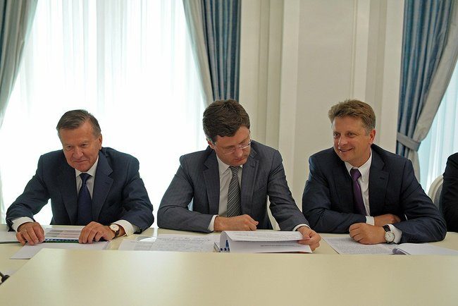Trzy osoby w garniturach dyskutują przy stole roboczym