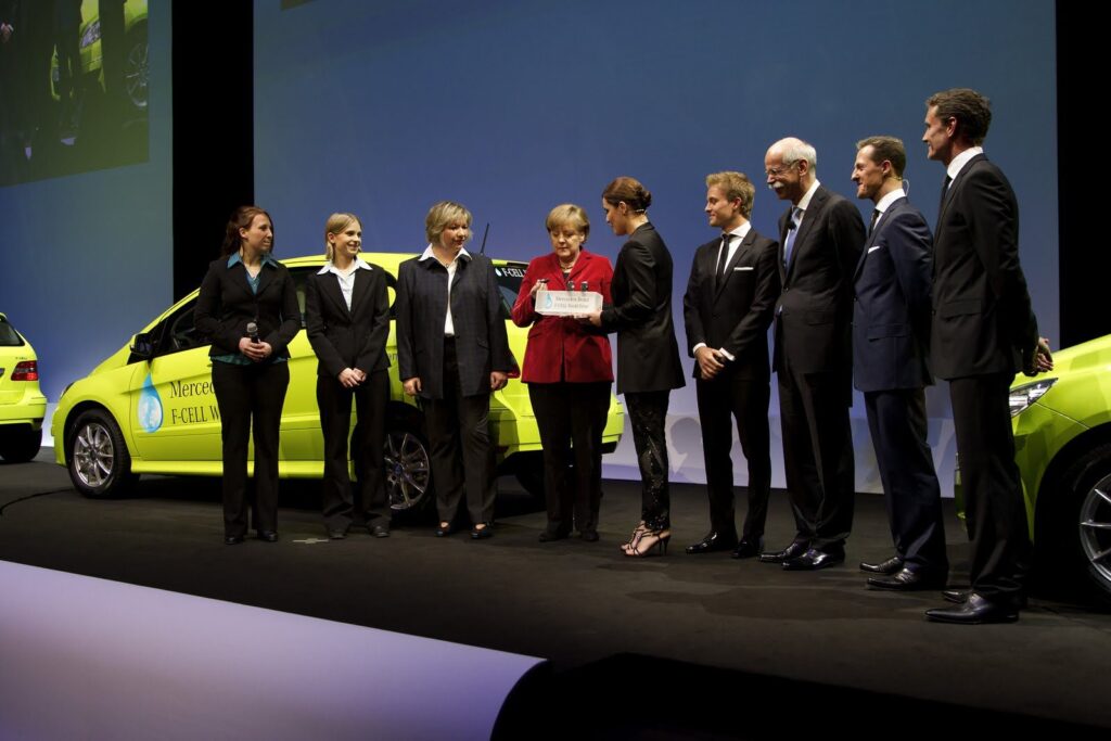 Angela Merkel i przedstawiciele Mercedes-Benz na scenie przy limonkowym Mercedesie B-Klasa F-Cell podczas prezentacji F-Cell World Drive